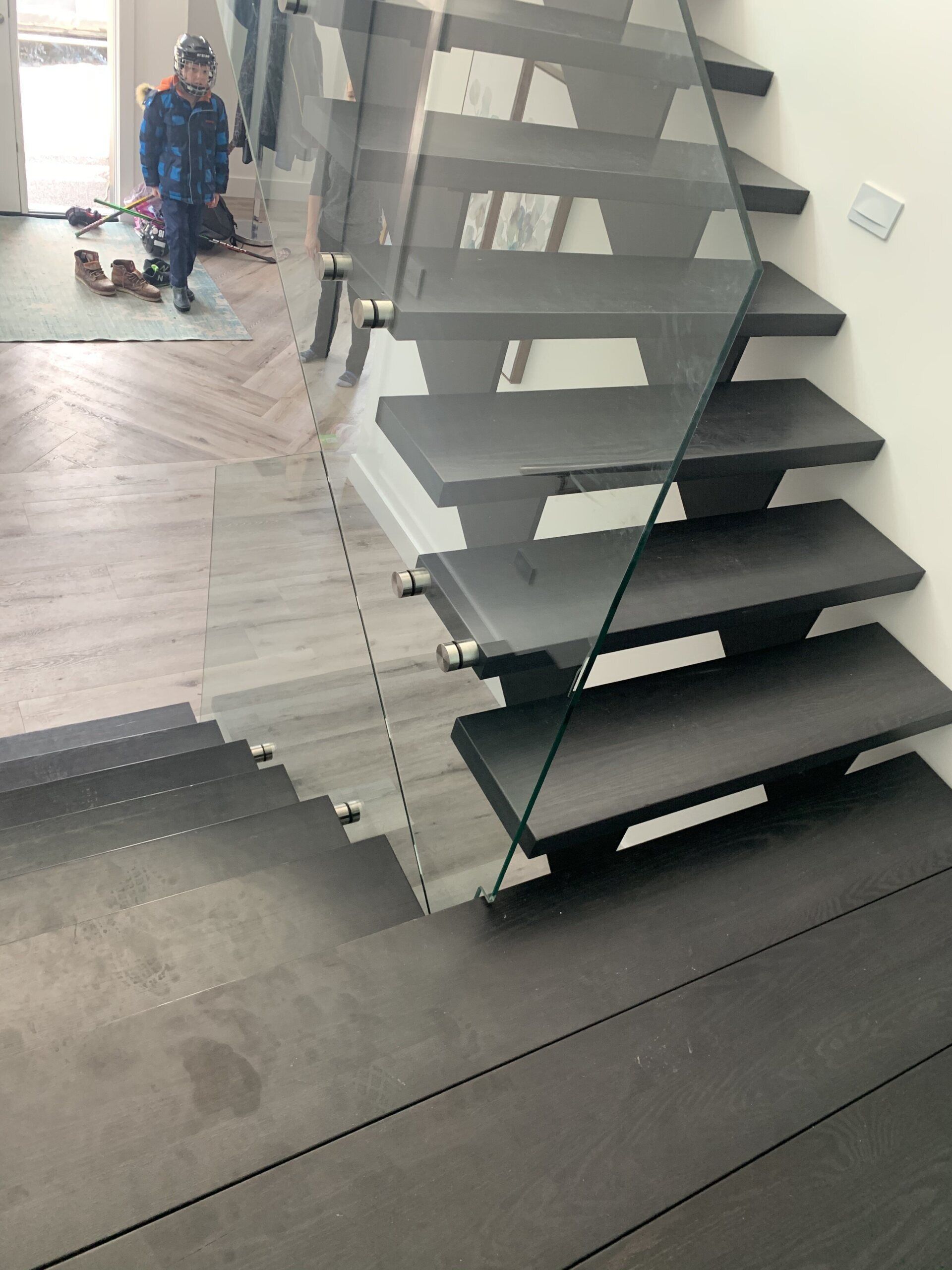 A child is standing next to a staircase with a glass railing.