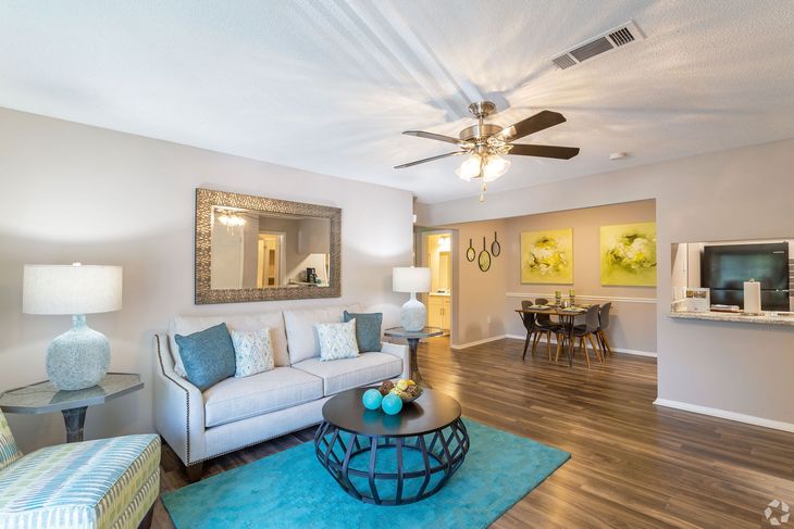 Living room with teal accents, sofa, coffee table, ceiling fan, and dining area visible.