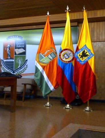 Se exhiben tres banderas en una habitación con un escudo de armas al fondo.