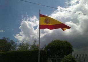 Una bandera española ondea al viento contra un cielo nublado.