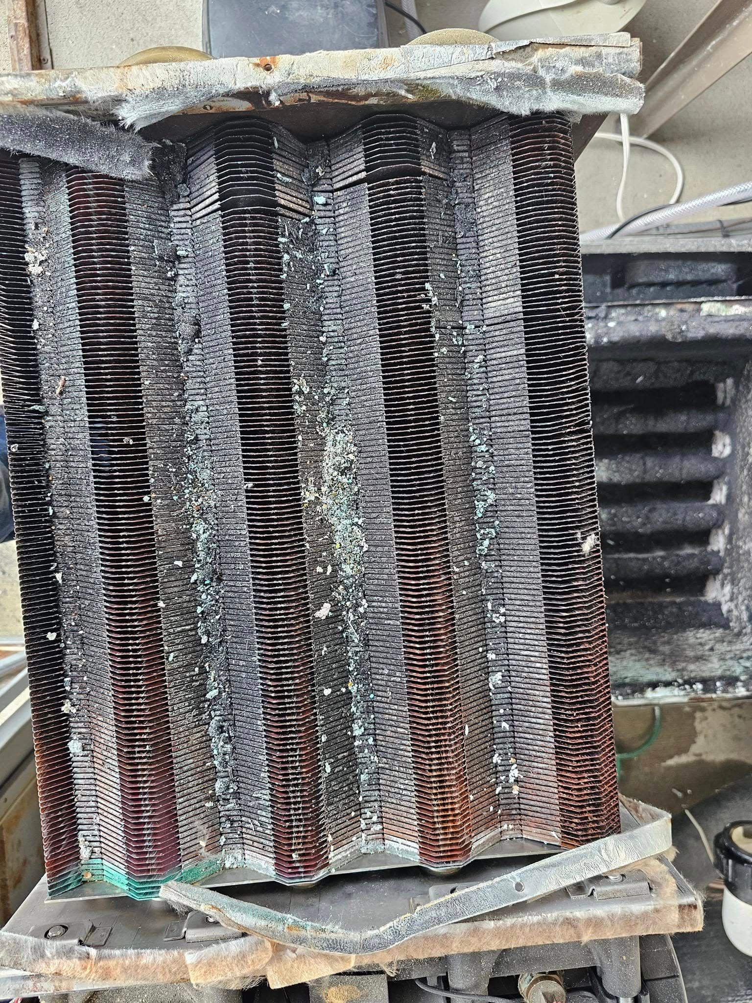 Corroded metal heat exchanger coil with numerous fins, possibly from an HVAC unit.