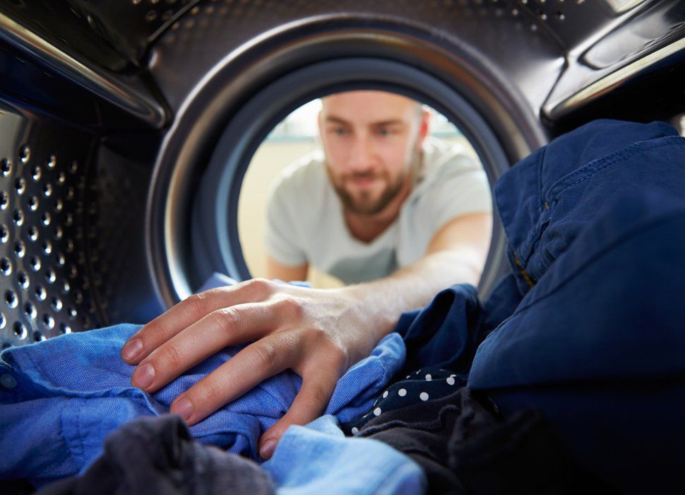 Laundry Service — Man Reaching A Shirt Inside Washing Machine in Holyoke, MA