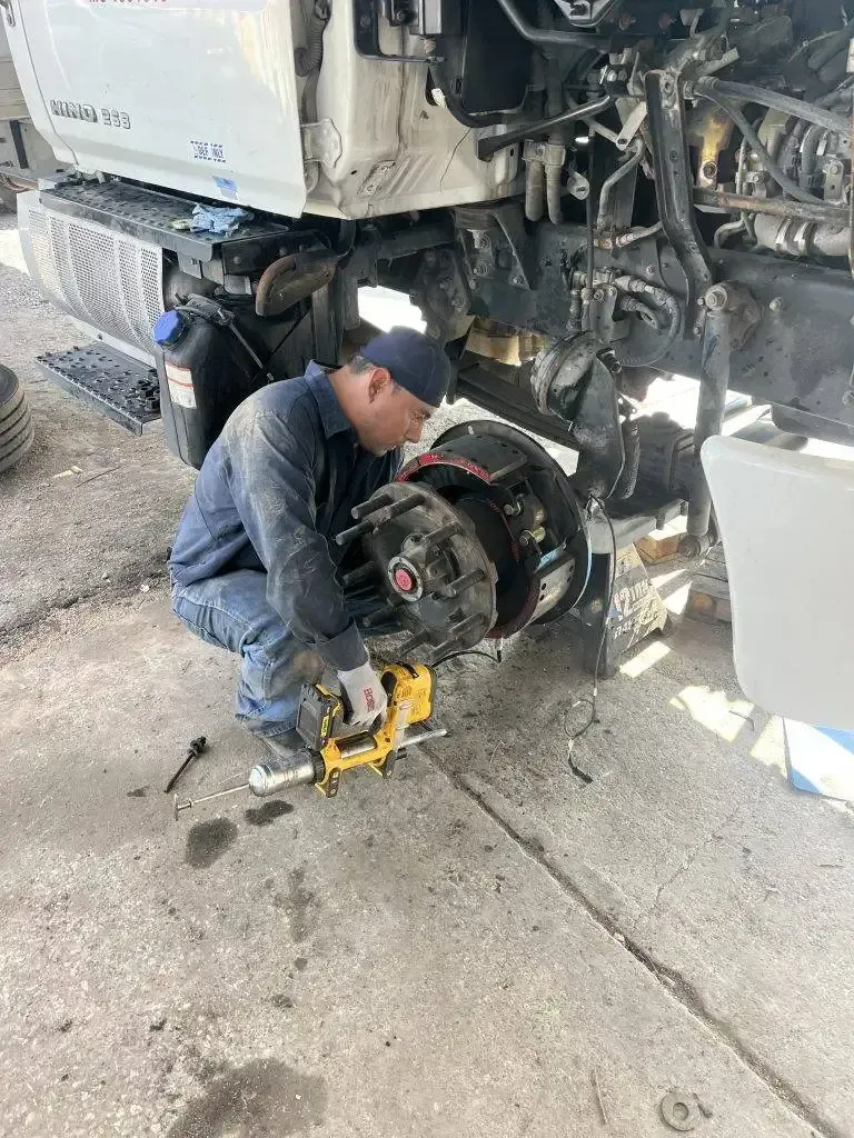 Mechanic works on truck's wheel. He is using a yellow power tool. 