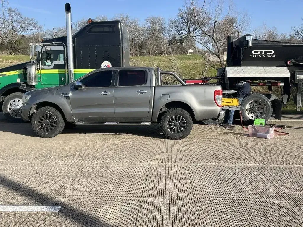 Gray truck with black wheels parked next to a semi-truck on a road.