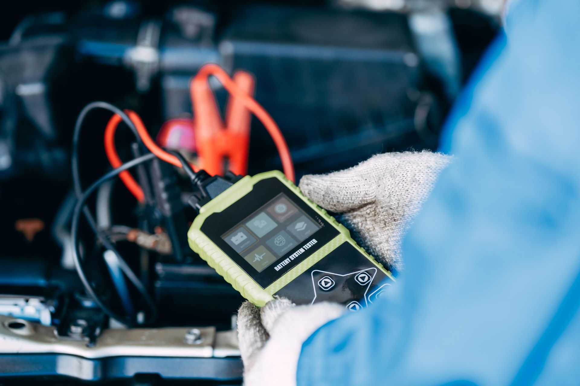 Mechanic using diagnostic tool on a car battery with jumper cables attached, engine bay.