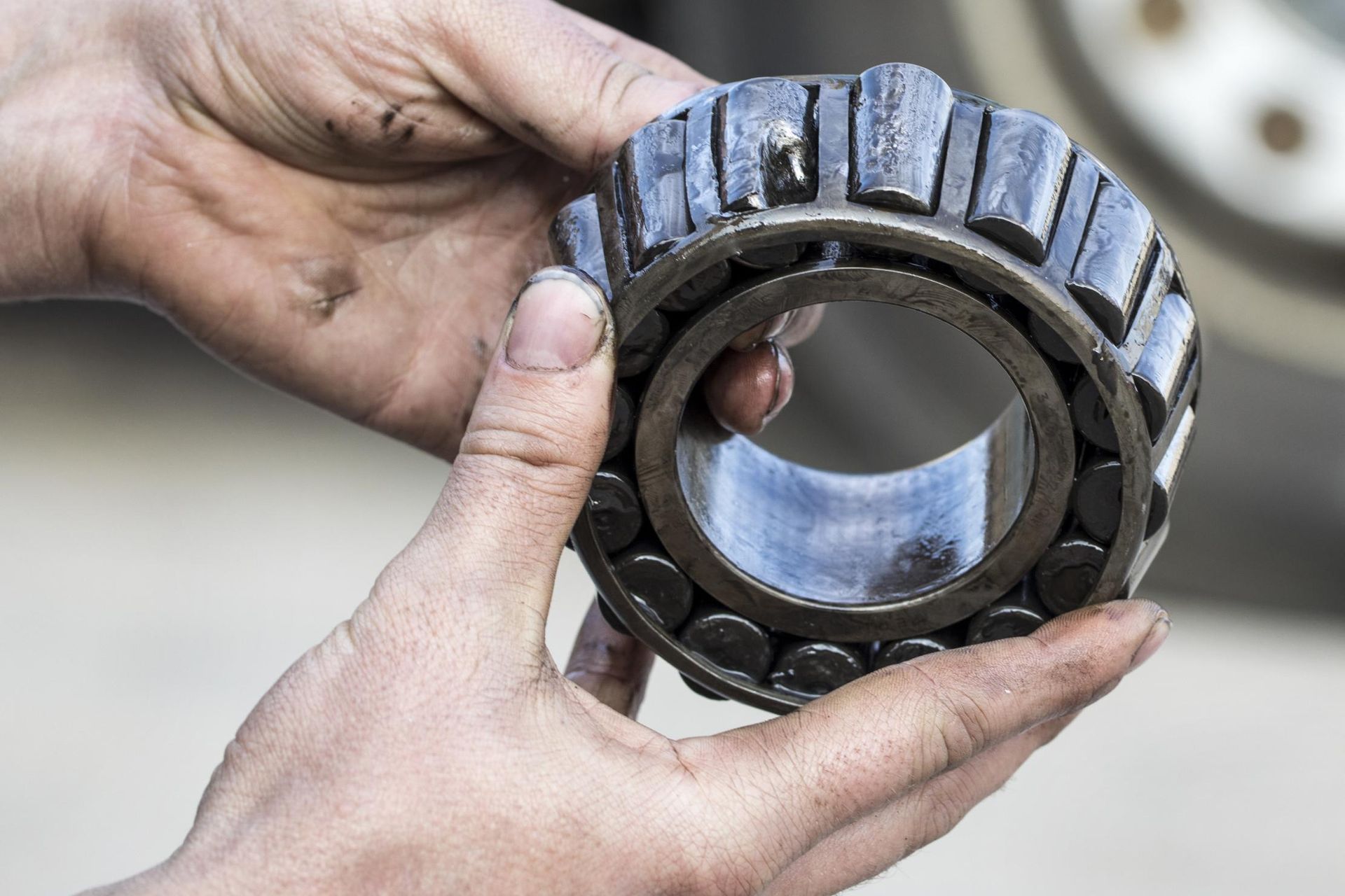Hands holding a used, oily bearing. Dark metal, grease, close-up shot.