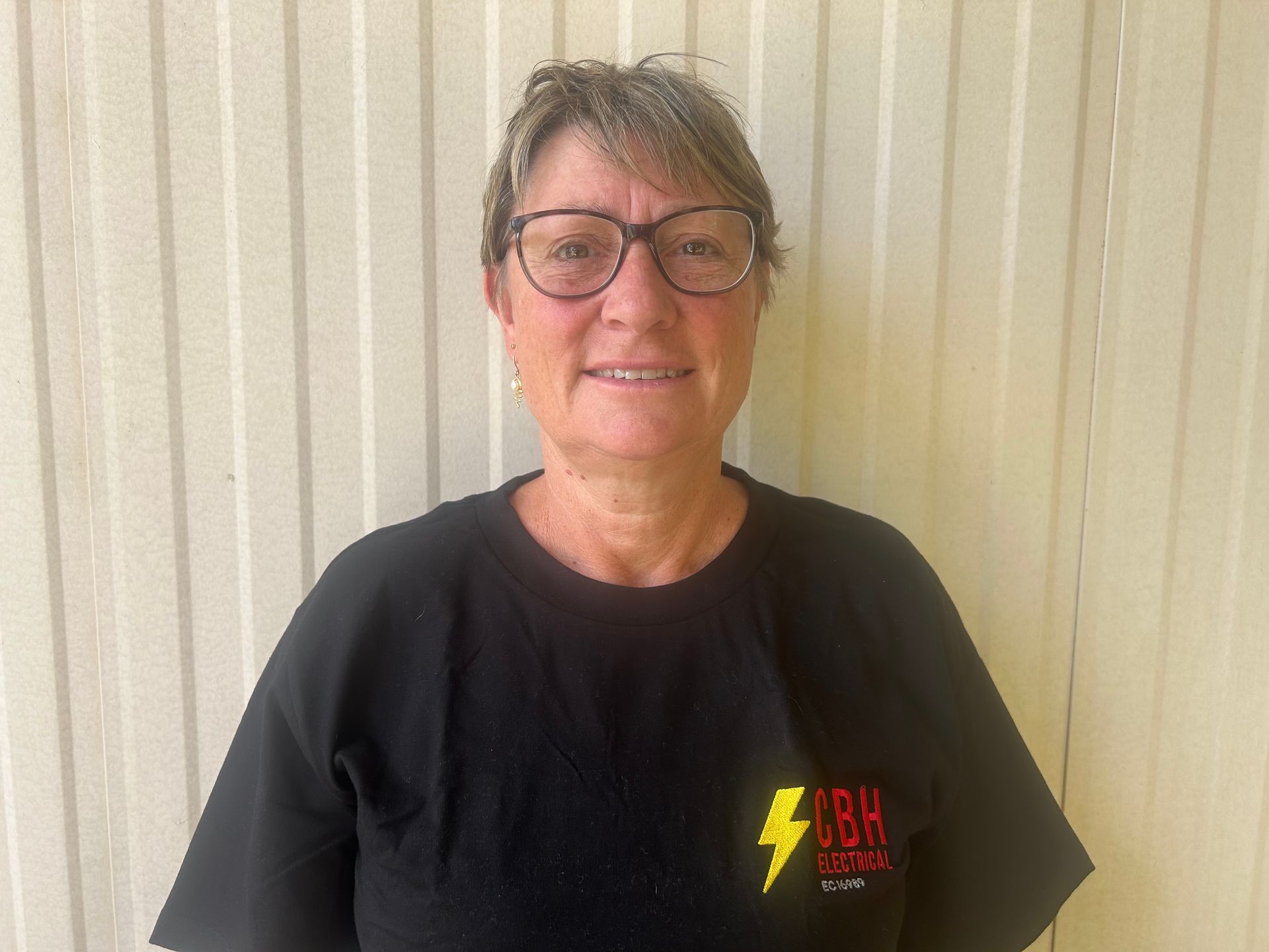 Woman wearing glasses and a black shirt stands in front of a neutral-colored wall.