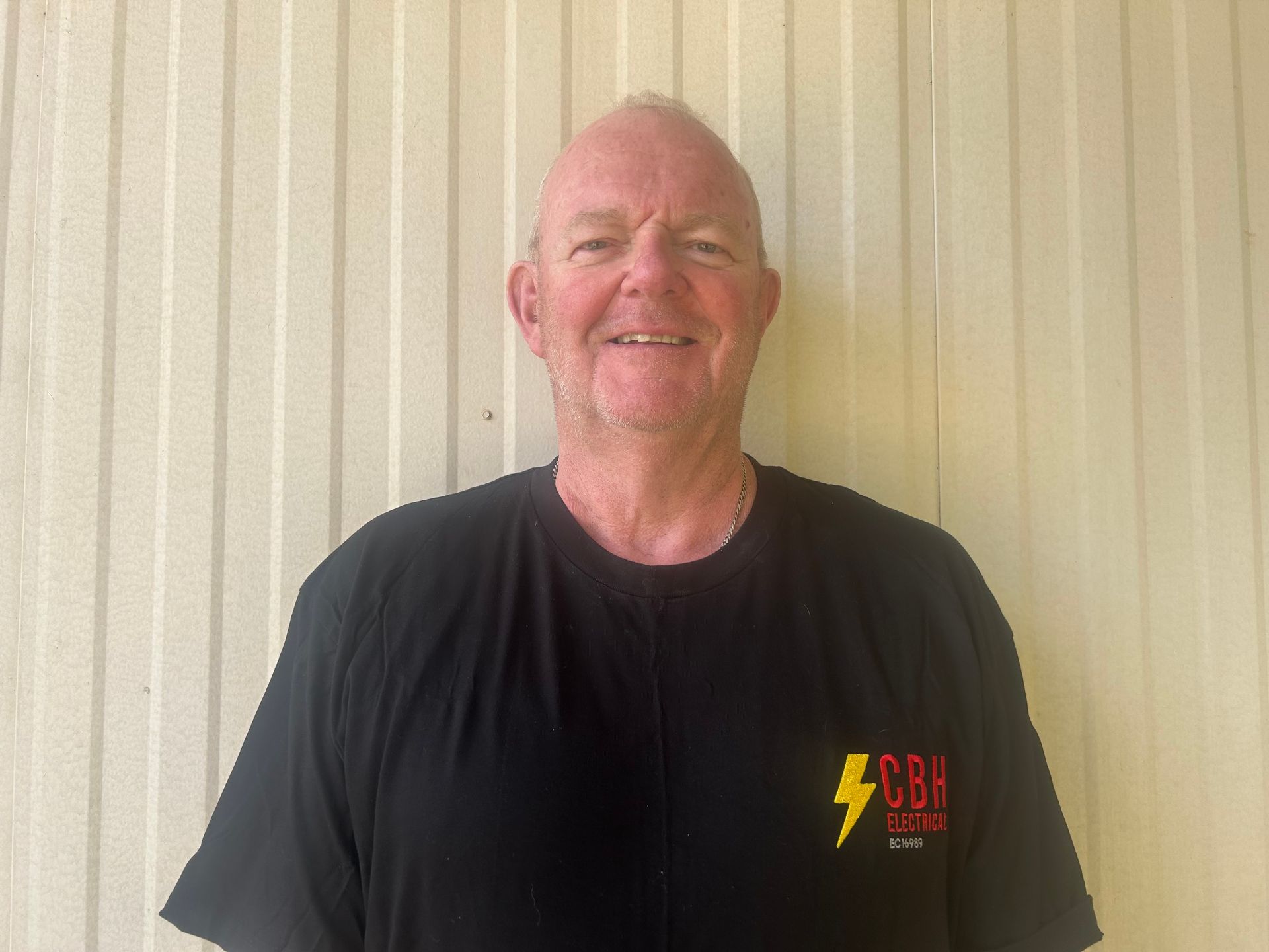 Man smiling, wearing a black t-shirt with a yellow lightning bolt and the letters