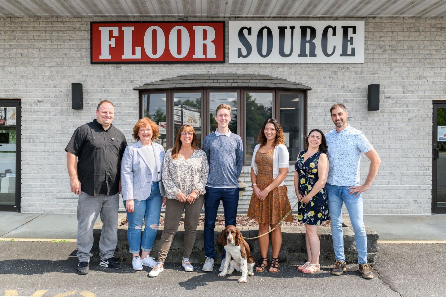 A group of people and a dog are posing for a picture in front of a floor source store.