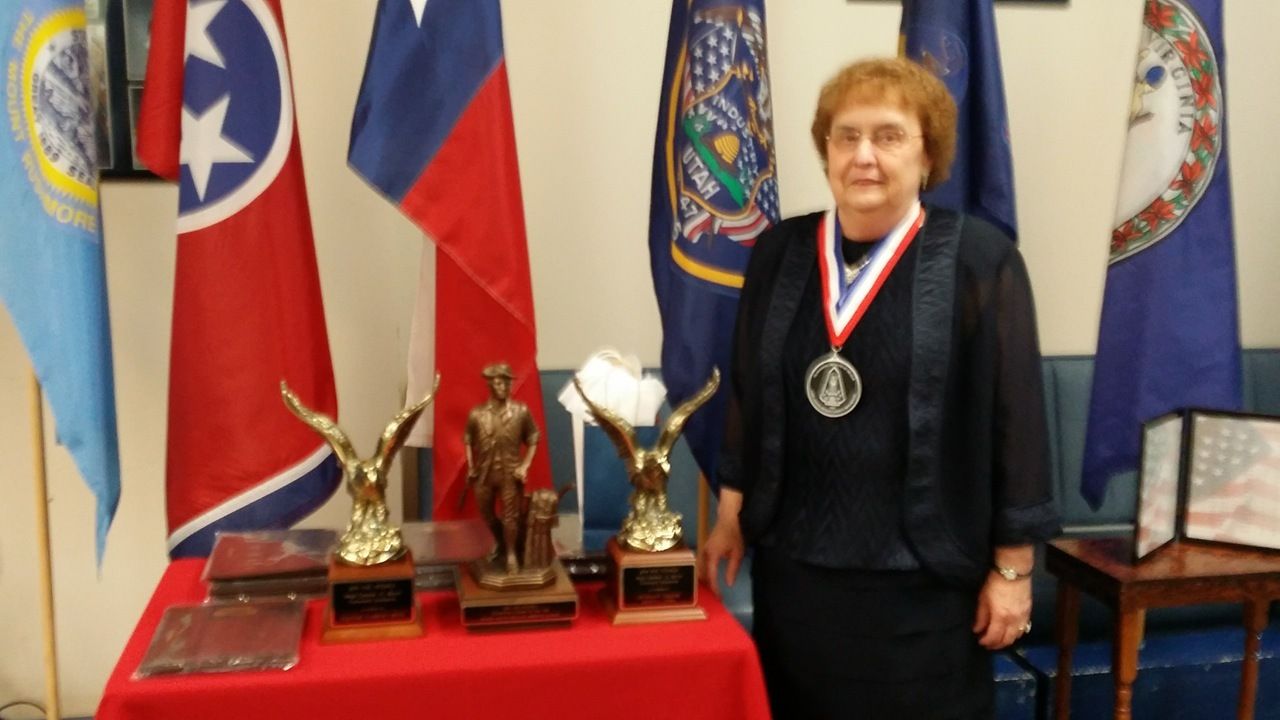 A woman wearing a medal is standing in front of flags and trophies