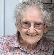 An elderly woman wearing glasses and a floral shirt is smiling for the camera.