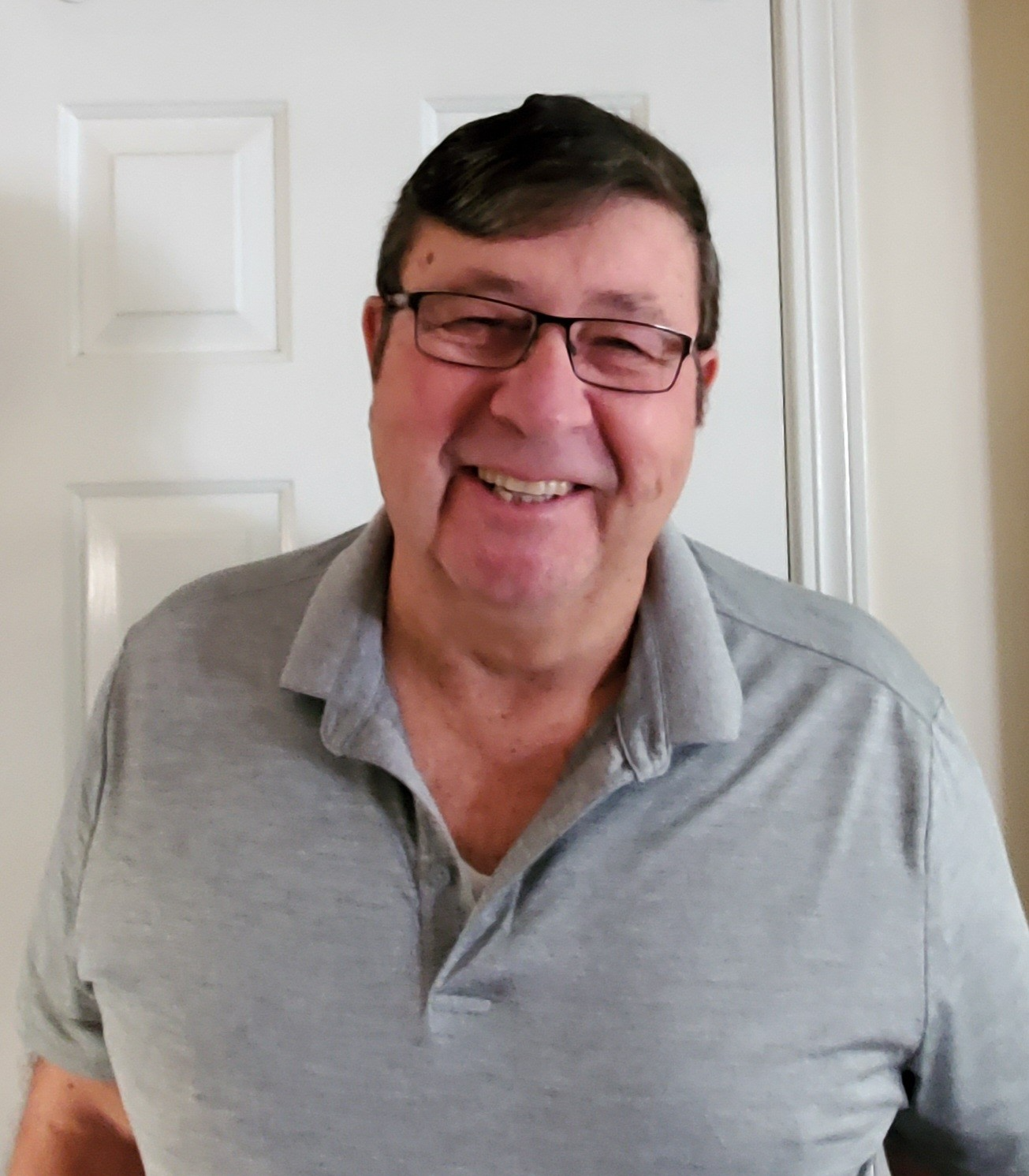 A man wearing glasses and a grey shirt is smiling