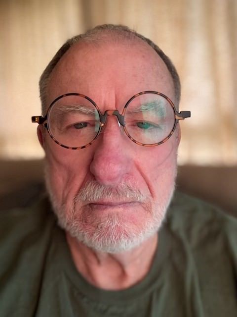 A man with glasses and a beard is sitting on a couch.