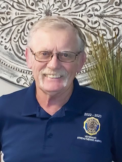 A man wearing glasses and a blue shirt is smiling for the camera.