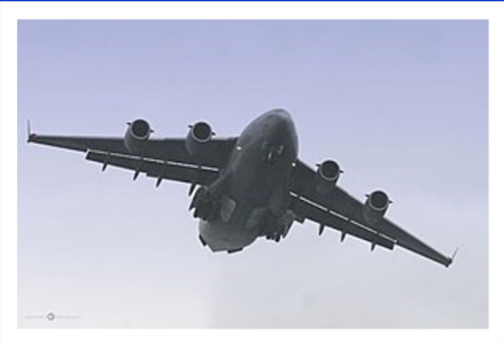 A large military plane is flying through a blue sky