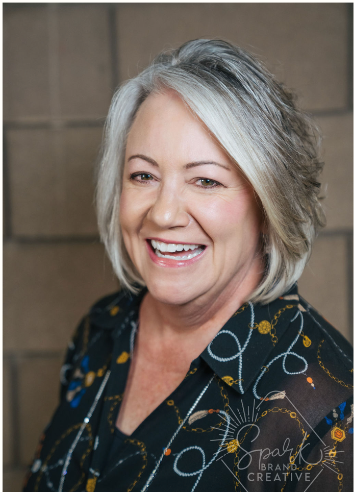 A woman with gray hair and a black shirt is smiling for the camera.