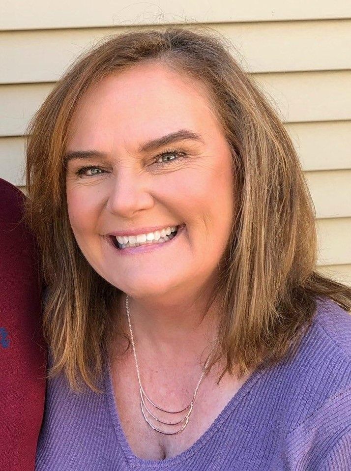 A woman in a purple shirt and necklace is smiling for the camera.