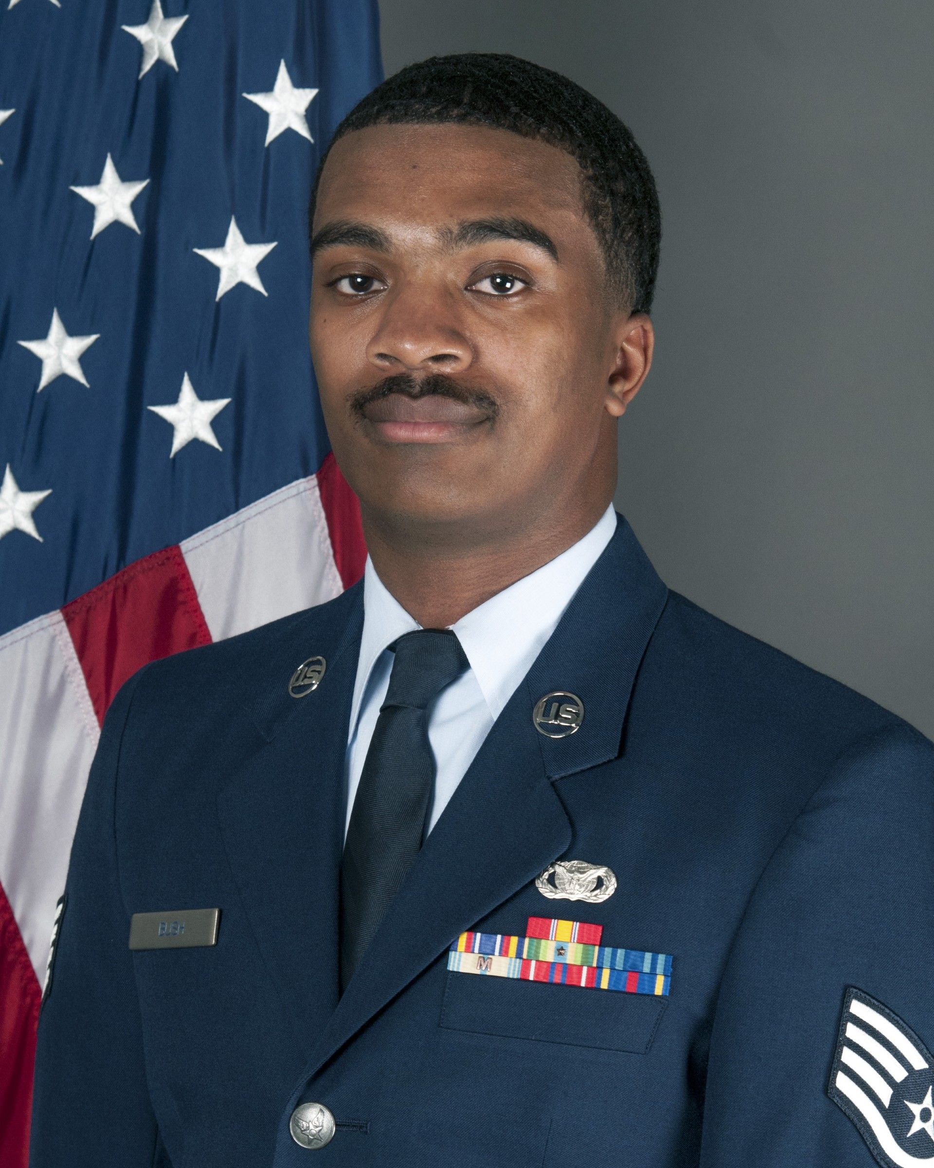 A man in a military uniform stands in front of an american flag