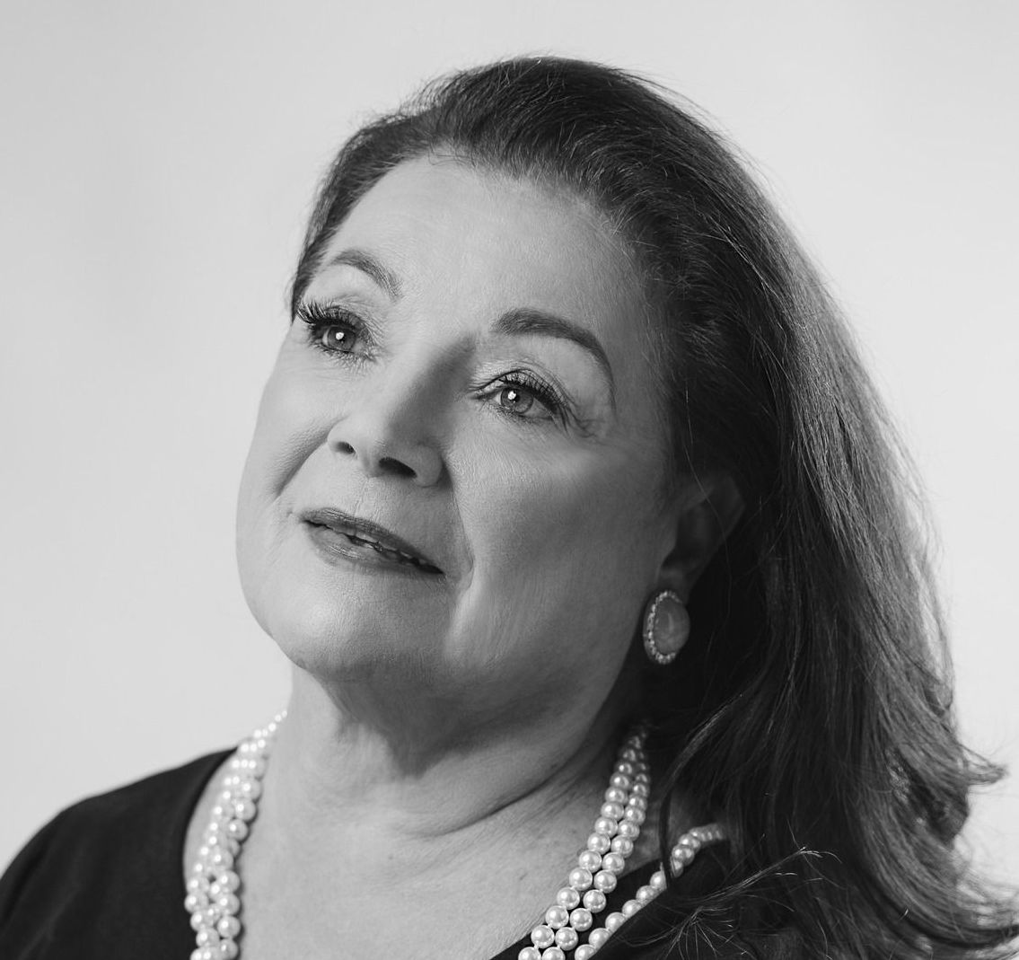A black and white photo of a woman wearing a pearl necklace and earrings.
