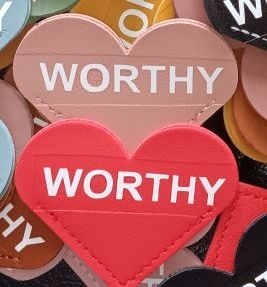 A red heart with the word worthy written on it is surrounded by other hearts.