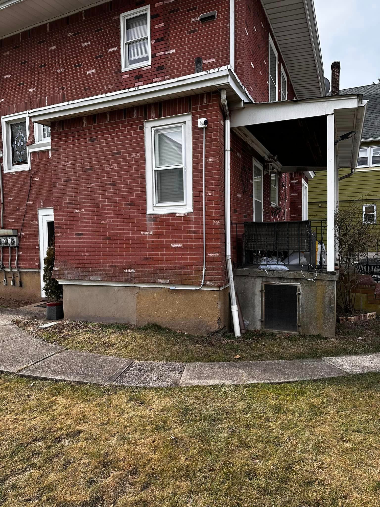 A red brick house with a porch and a sidewalk in front of it.