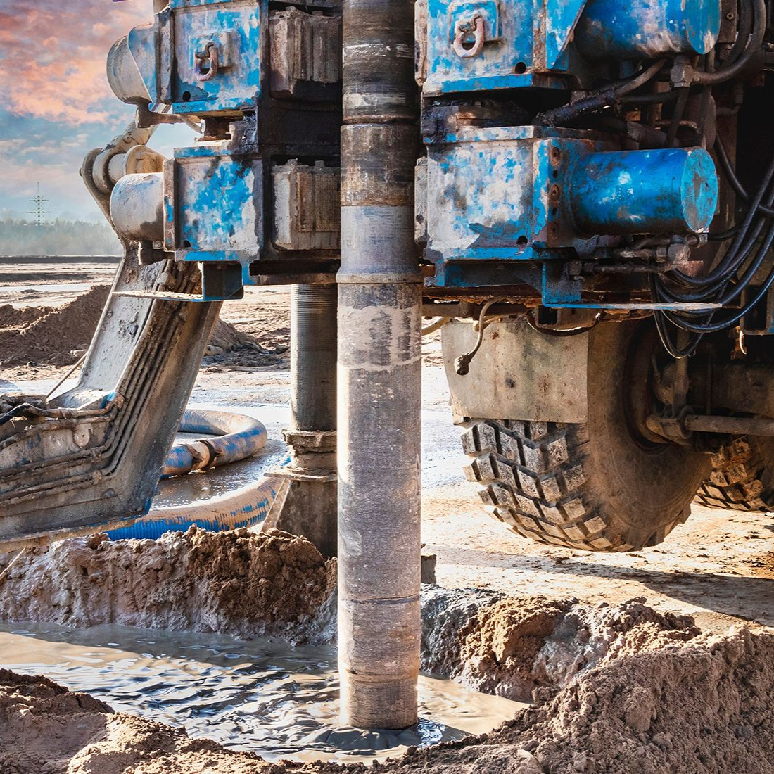 Blue drilling rig working in a muddy, outdoor setting.