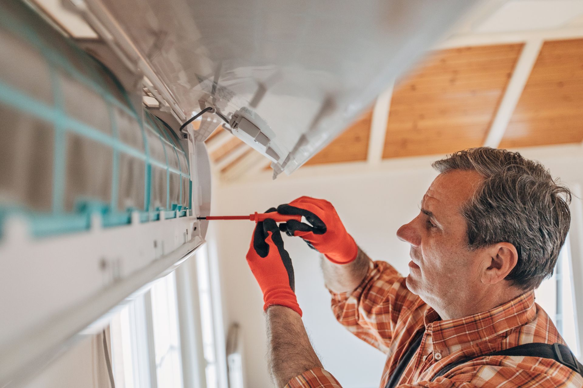 A man is fixing an air conditioner with a screwdriver.