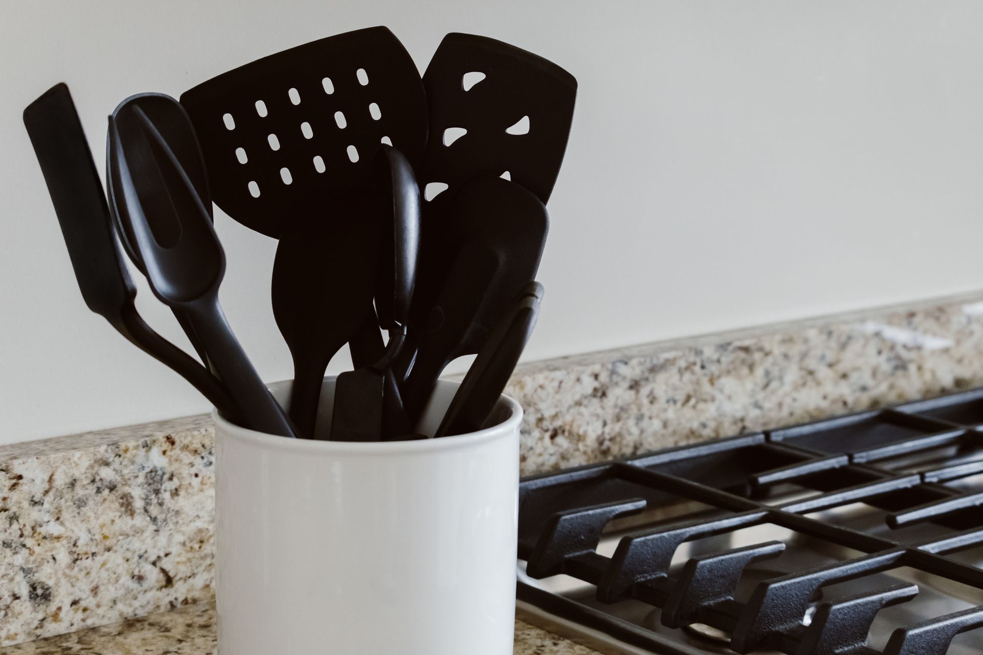 A white container filled with black kitchen utensils is sitting on a stove.