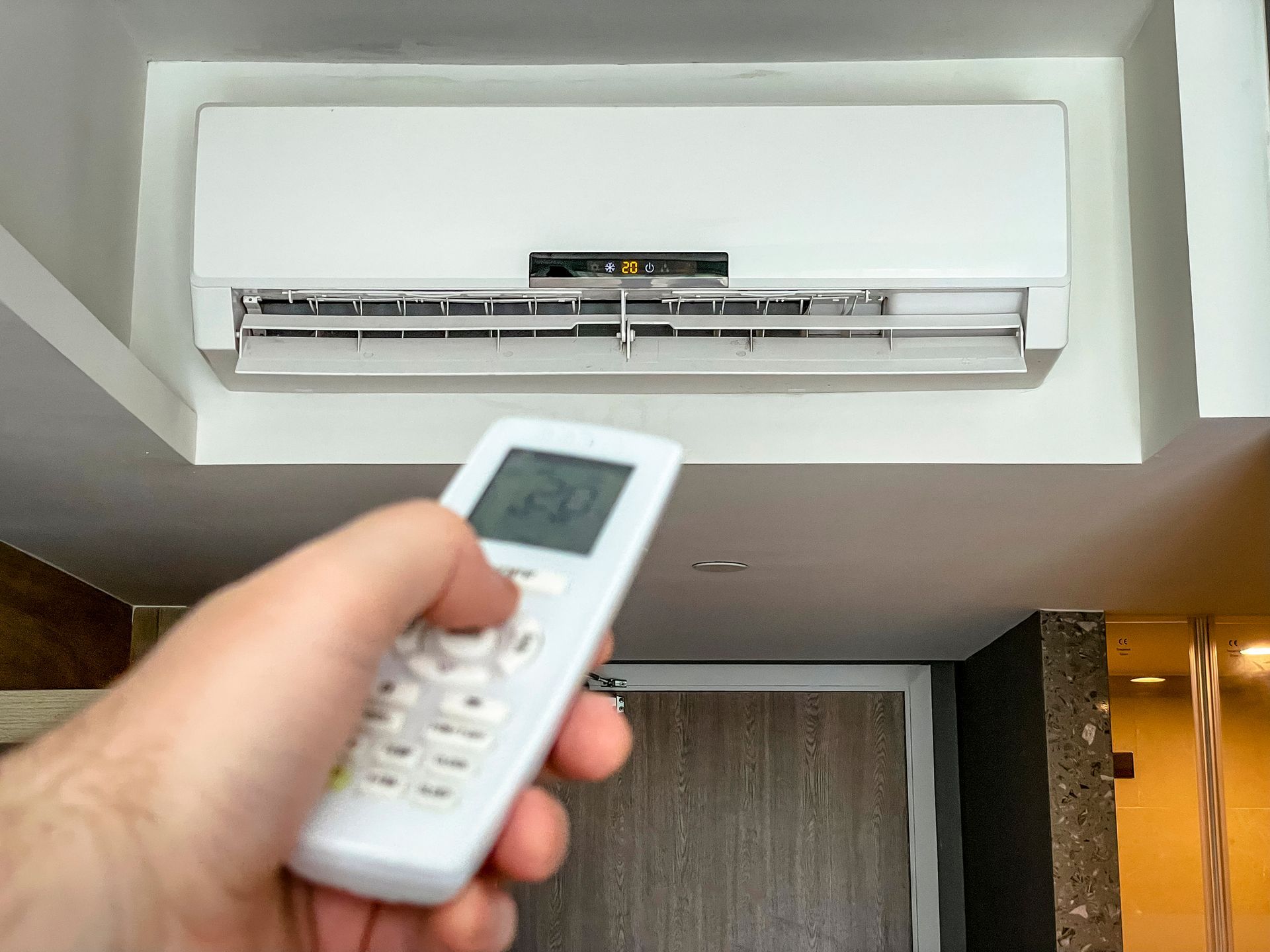 A person is holding a remote control in front of an air conditioner.