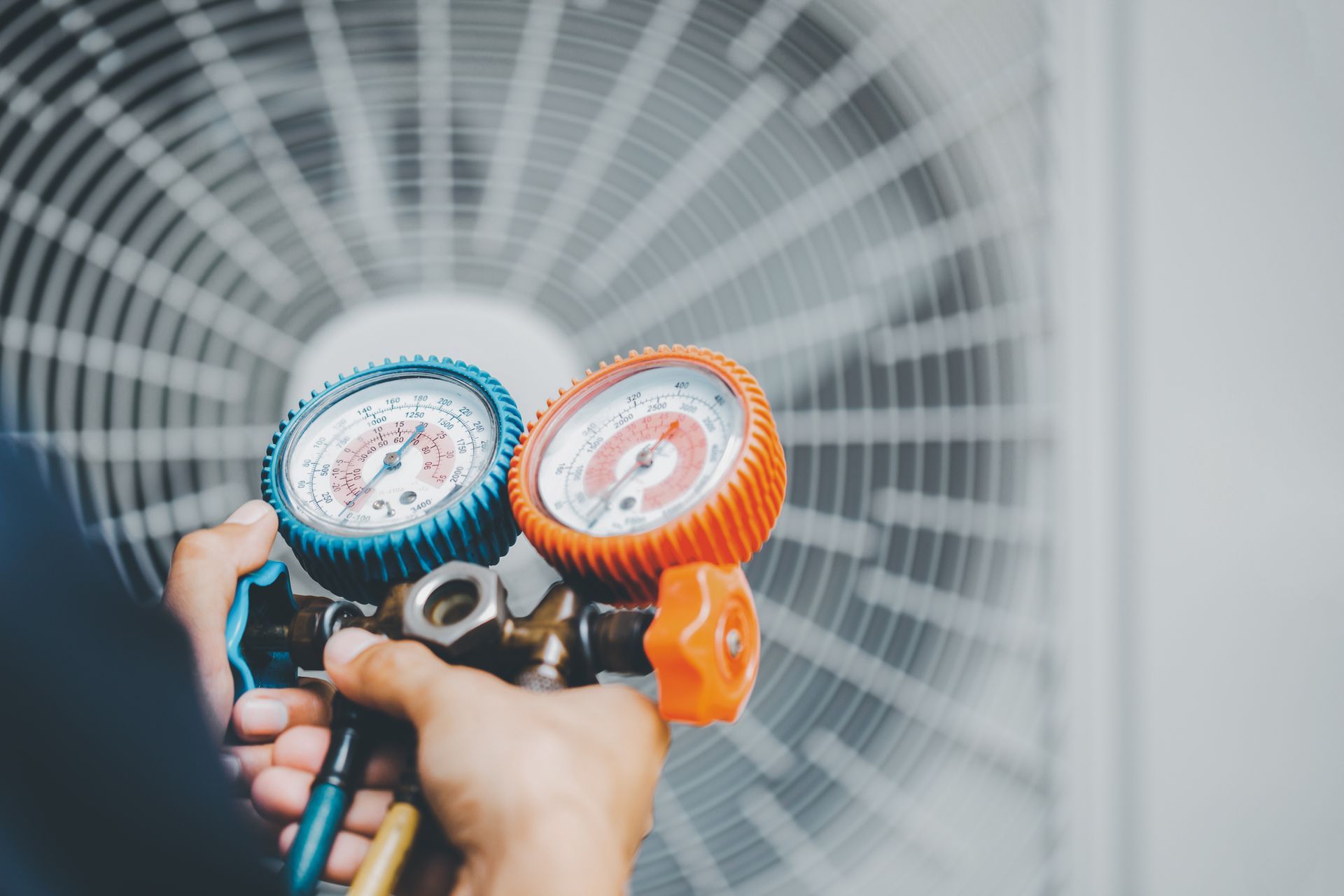 A person is holding two gauges in front of an air conditioner.