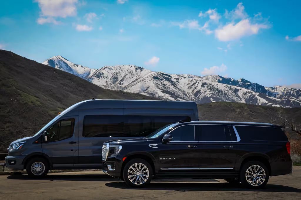 A van and a suv are parked next to each other in front of a mountain.