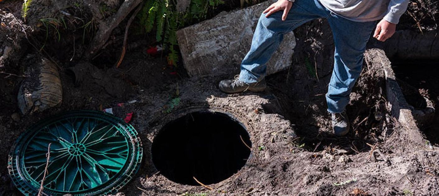 a man is standing in the dirt next to a manhole cover .