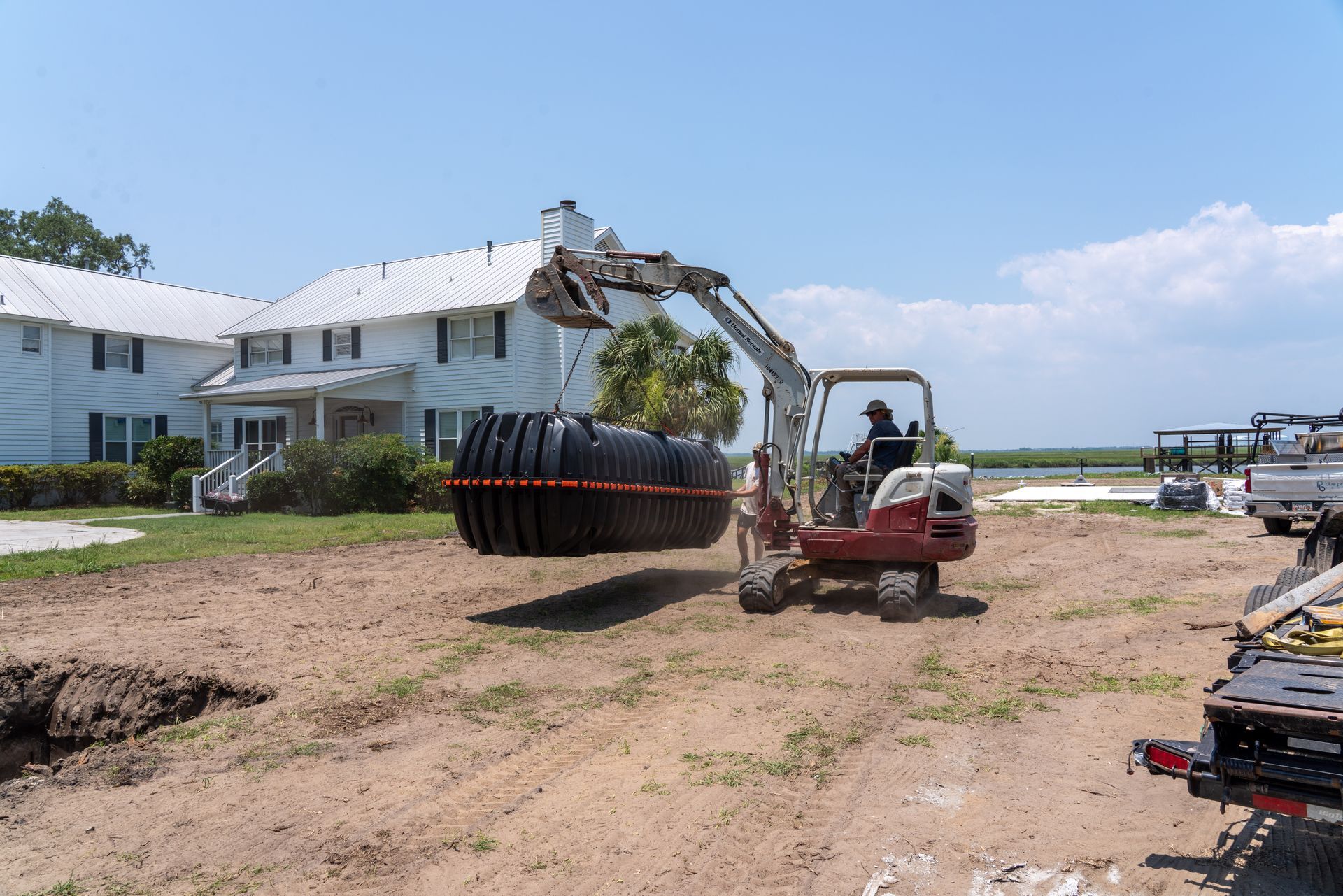 an excavator is carrying a large black tank in front of a house