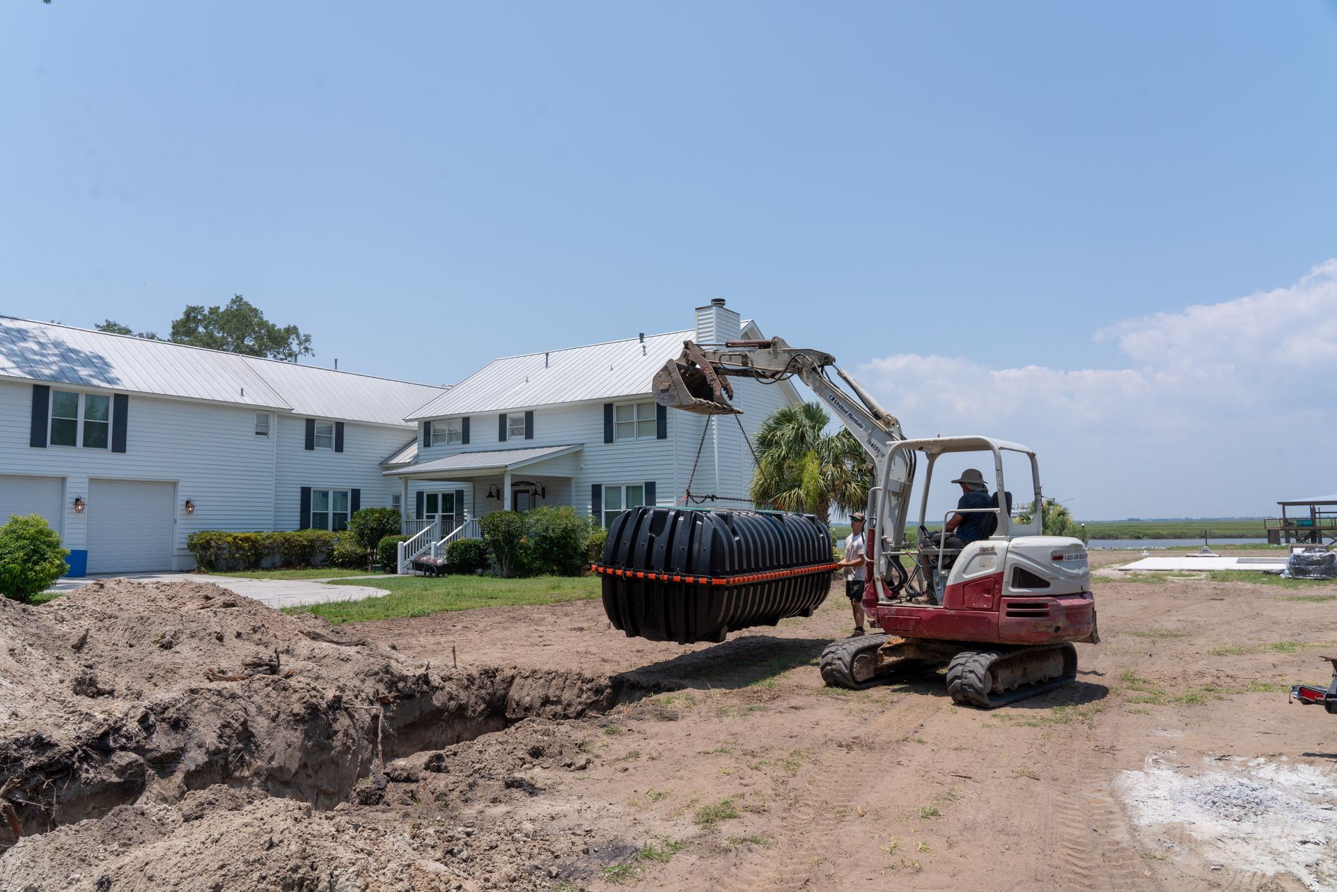 an excavator is carrying a large tank in front of a house