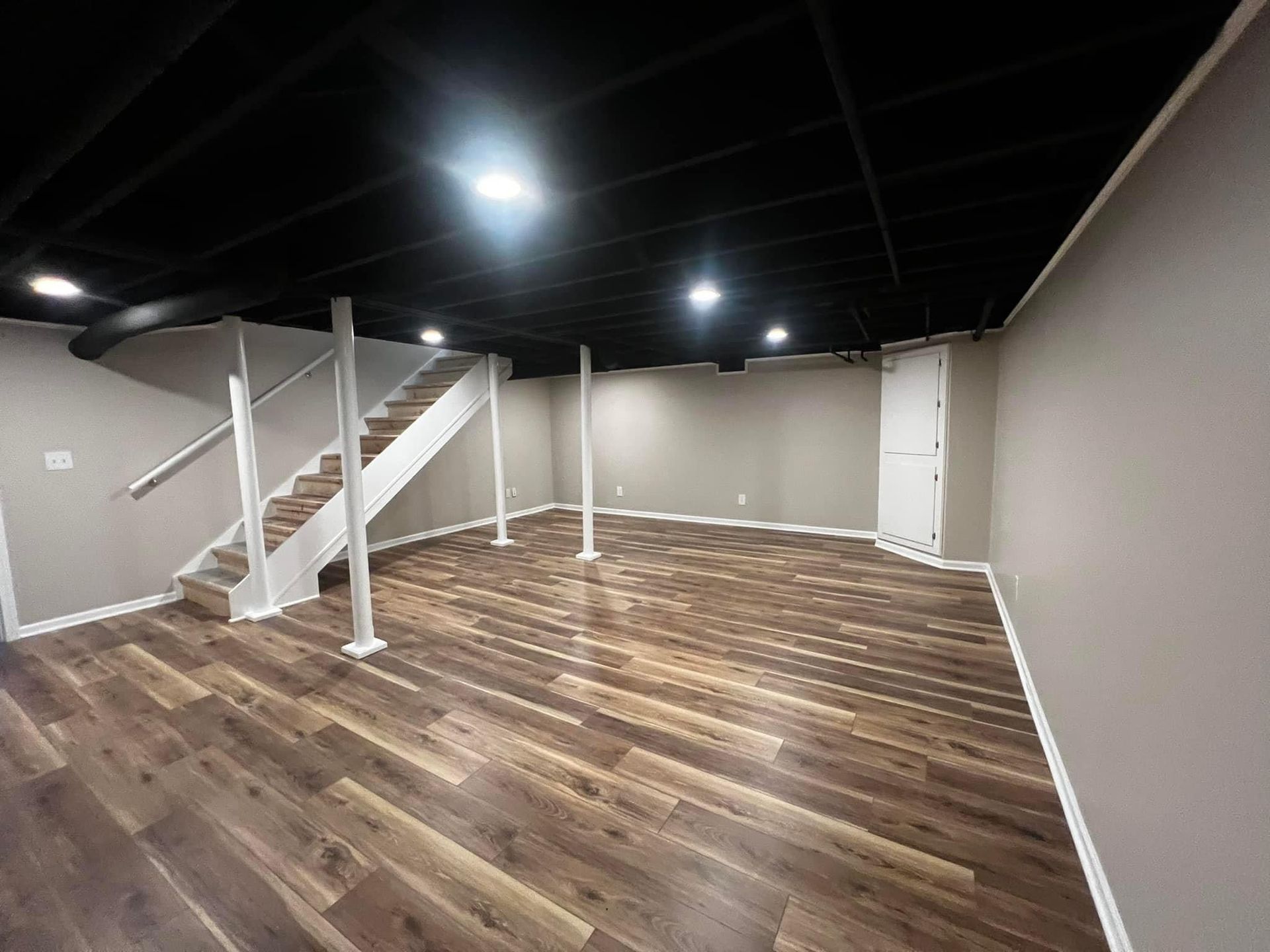 An empty basement with hardwood floors and stairs.