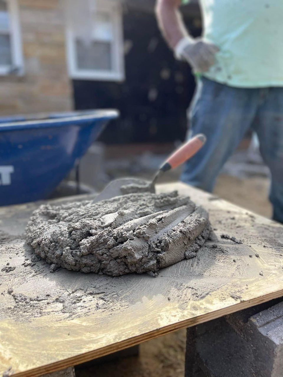 A person is spreading concrete on a wooden board with a trowel.
