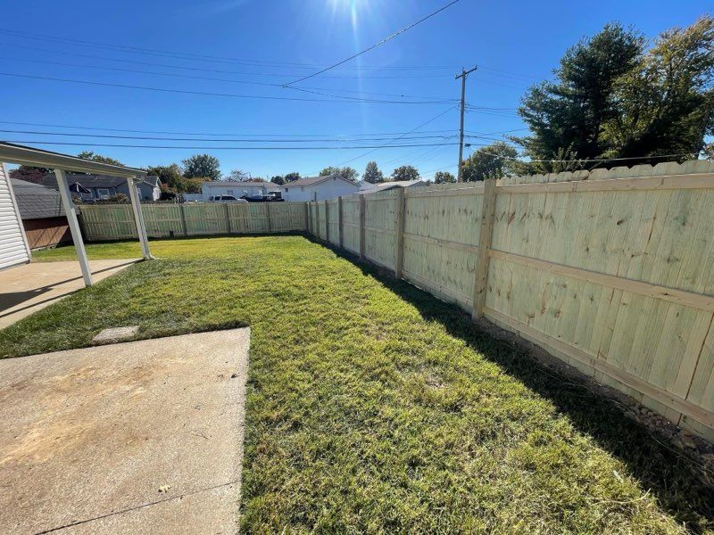 A backyard with a wooden fence and a concrete driveway.