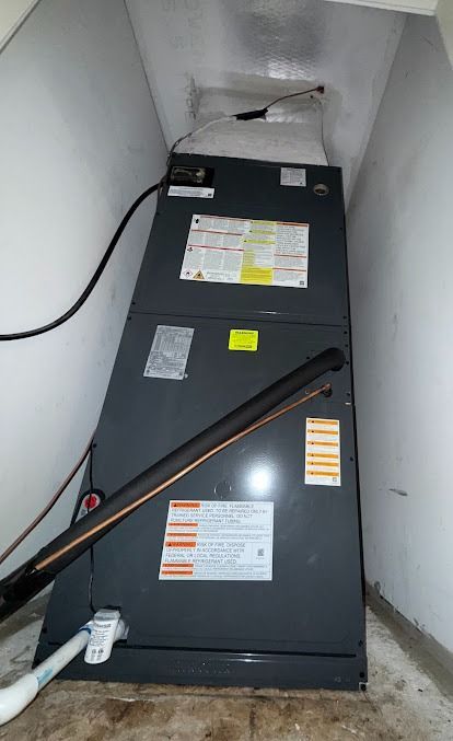 Black HVAC air handler unit in a narrow closet with labels and exposed wires.