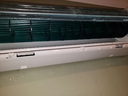 Close-up of a wall-mounted air conditioner with its front panel open and dark filter visible.
