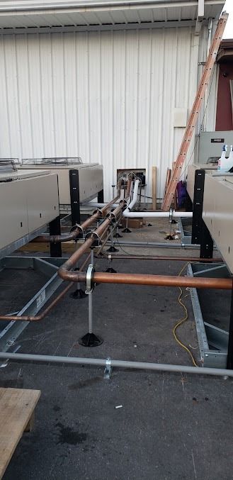 Trailer chassis in an outdoor lot beside a white building, with metal frame, jack stand, and equipment mounted on top.