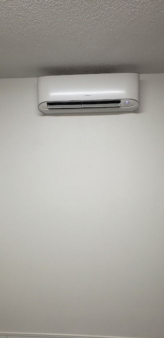 Wall-mounted white air conditioner near the ceiling on a plain white wall.