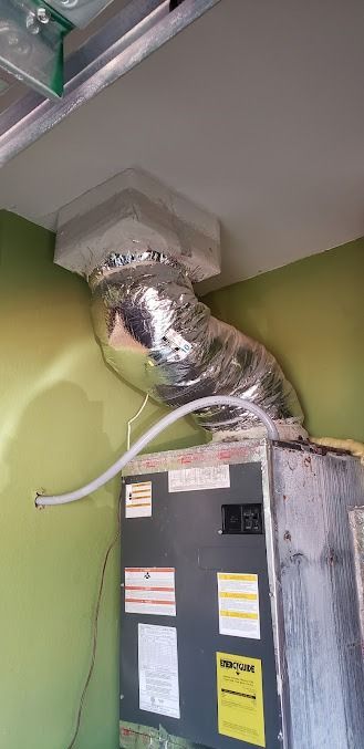Flexible duct attached to a gray HVAC unit in a green mechanical room ceiling corner