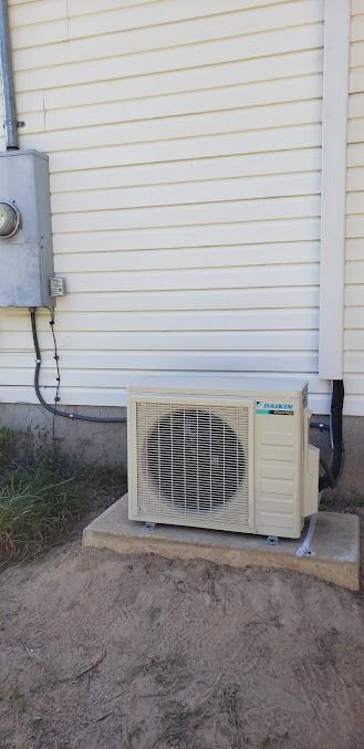 Outdoor air conditioning unit beside a beige house wall with utility meter and conduit attached