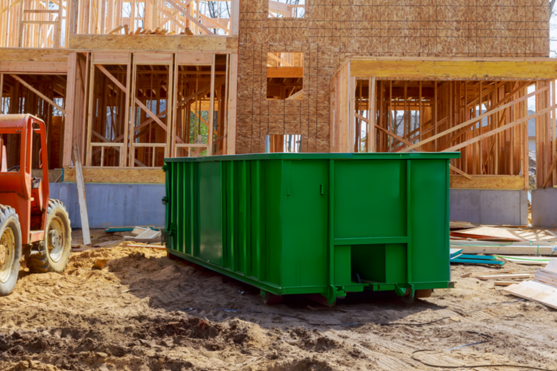 A green dumpster is parked in front of a house under construction.