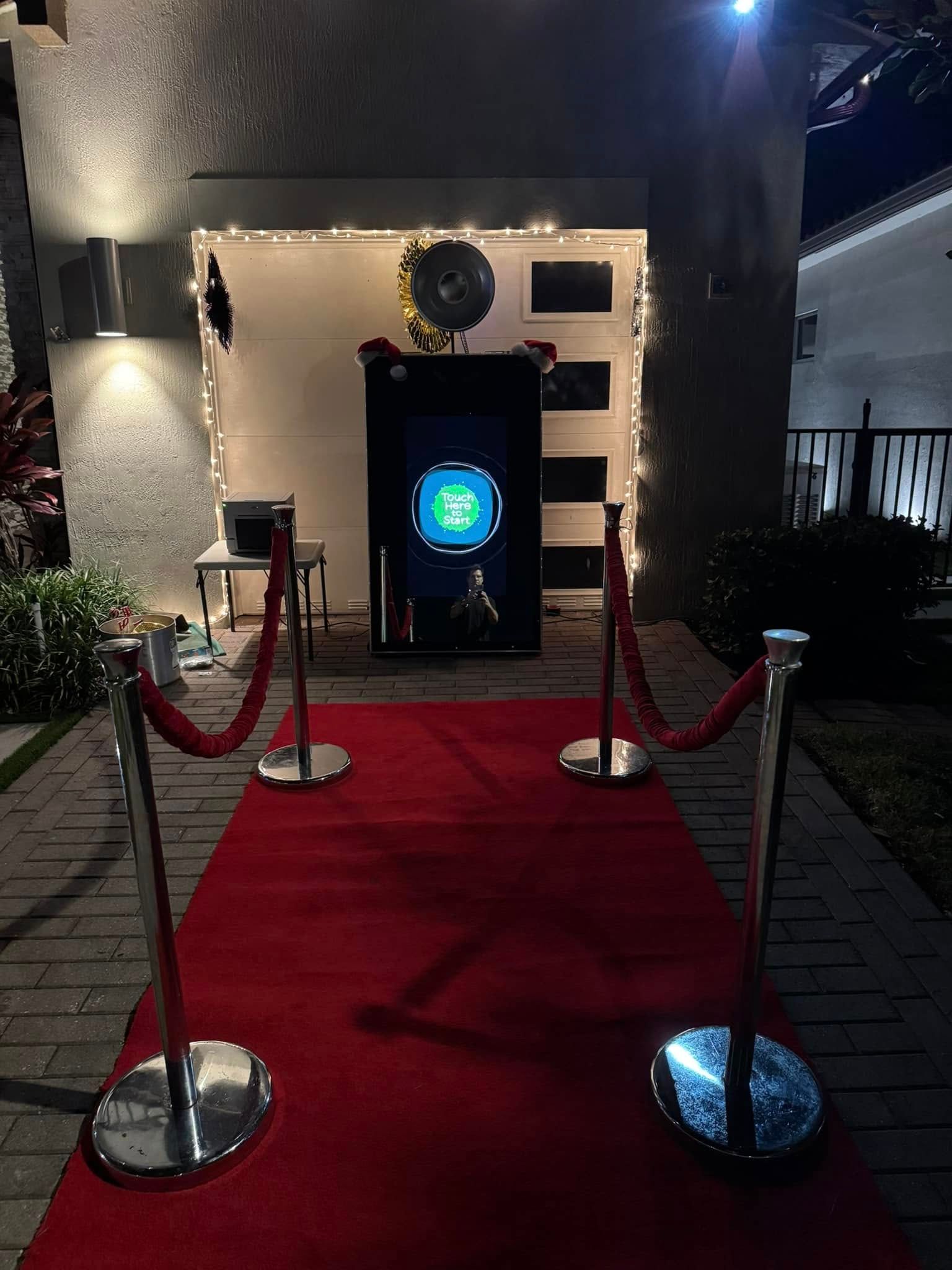 Red carpet leading to a photo booth at an outdoor event. Stanchions with ropes create a pathway.