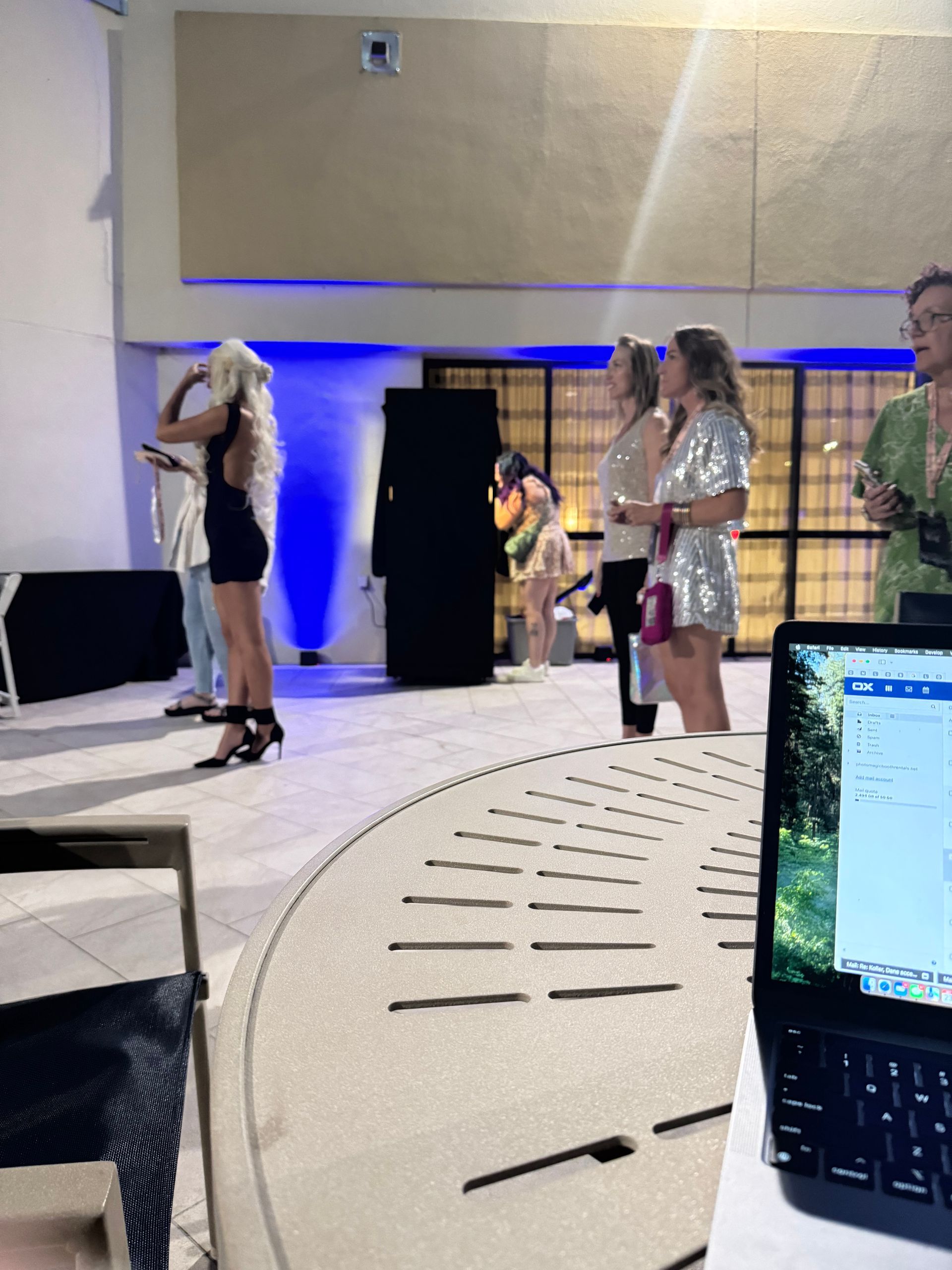 People standing indoors, some holding microphones. A laptop sits on a table in the foreground.