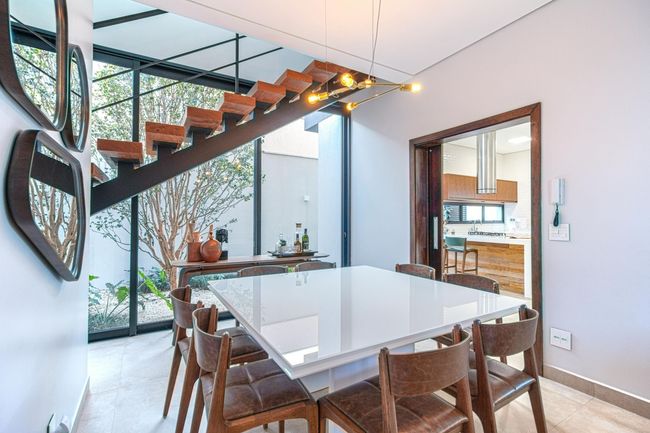 Salle à manger moderne avec table en verre, chaises en bois et escalier suspendu près de grandes fenêtres