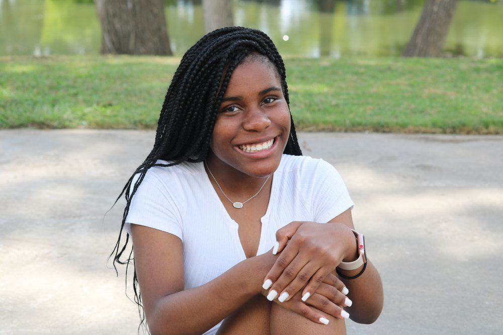 A woman is sitting on the ground with her legs crossed and smiling.