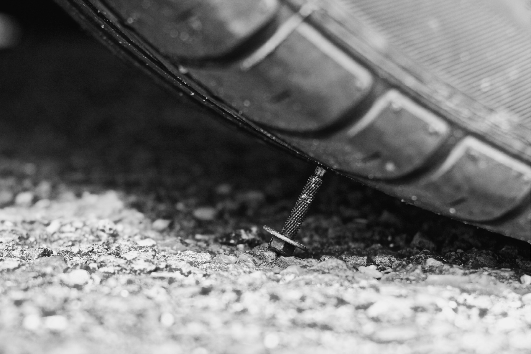 A black and white photo of a tire with a nail sticking out of it.