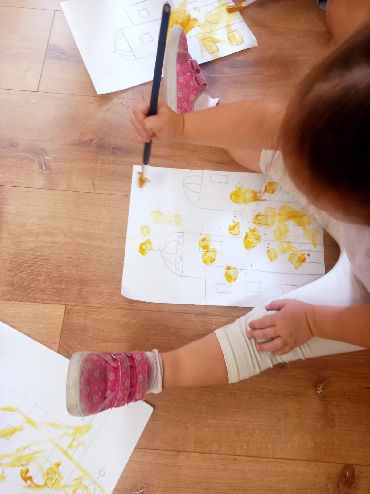 Una bambina è seduta sul pavimento e dipinge con un pennello